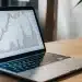 AI stock prediction app on smartphone with stock charts on laptop.