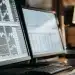 AI trading software displayed on dual monitors with charts, data, keyboard, and coffee.